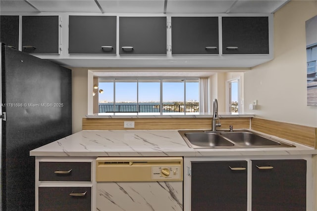 kitchen featuring a sink, freestanding refrigerator, light stone counters, and dishwashing machine