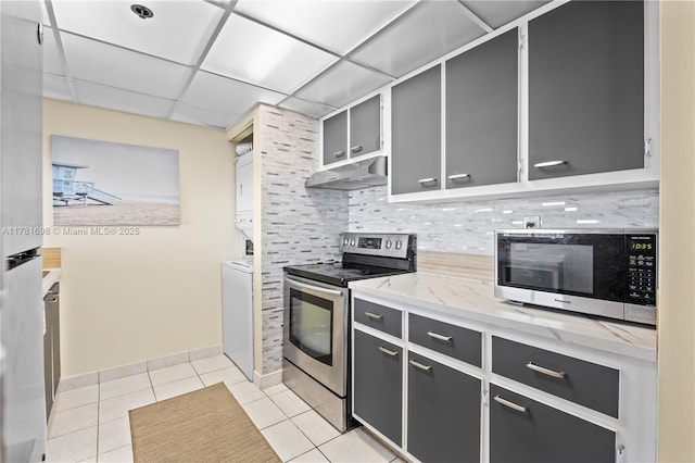 kitchen with stacked washer and dryer, backsplash, light tile patterned flooring, under cabinet range hood, and stainless steel appliances