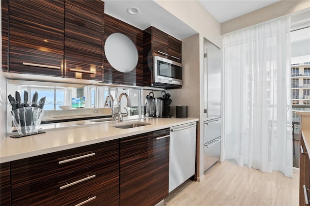 kitchen with a sink, modern cabinets, dark brown cabinetry, light countertops, and appliances with stainless steel finishes