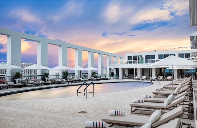 pool at dusk with a community pool, a patio, and an outdoor living space