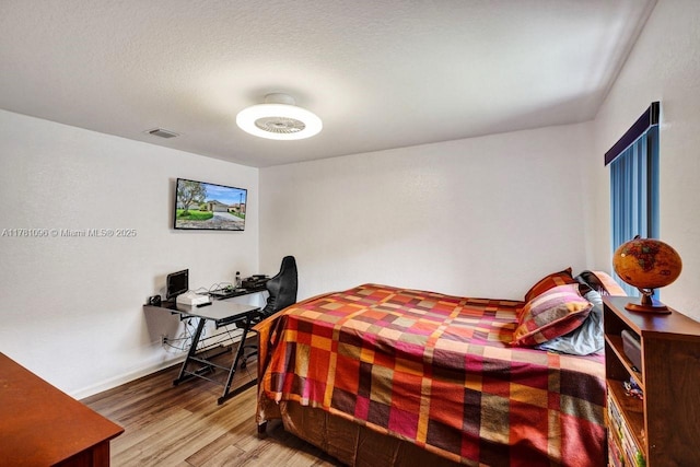 bedroom with baseboards, visible vents, and wood finished floors