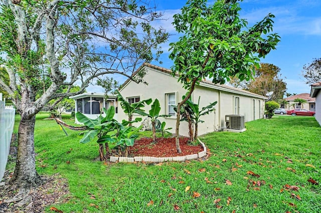 view of side of property with a sunroom, stucco siding, a yard, and central AC