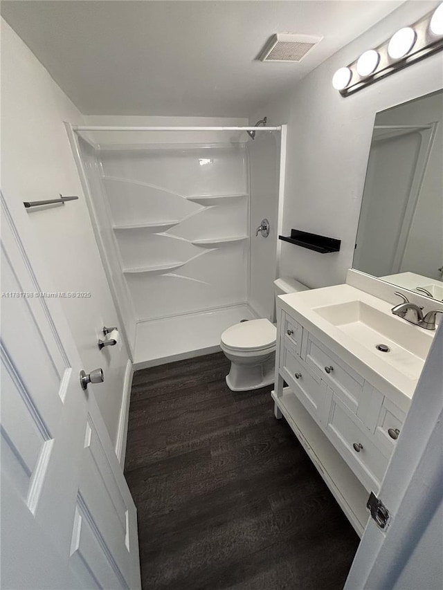 bathroom with visible vents, toilet, vanity, wood finished floors, and a stall shower