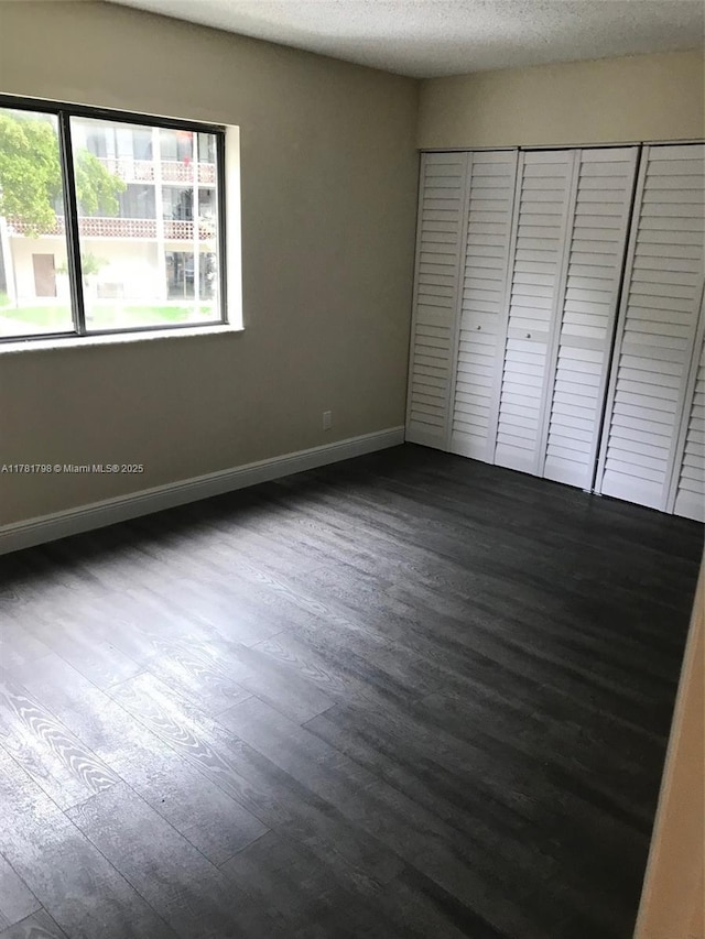 unfurnished bedroom featuring a textured ceiling, a closet, baseboards, and dark wood finished floors
