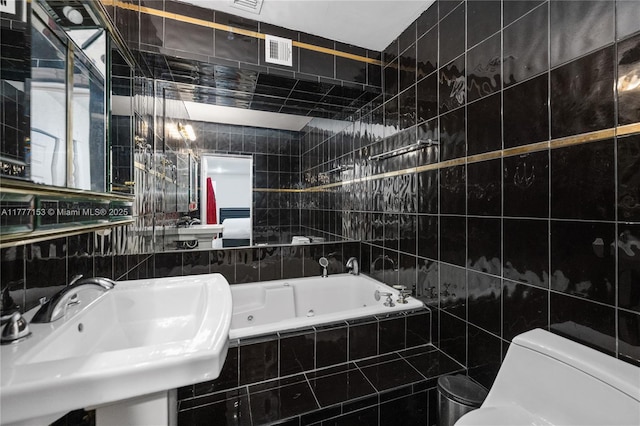 full bathroom with visible vents, a sink, tile walls, toilet, and a whirlpool tub