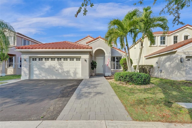 mediterranean / spanish-style home featuring a tiled roof, aphalt driveway, a garage, and stucco siding