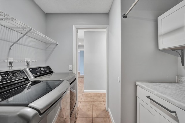 washroom with a textured ceiling, light tile patterned flooring, baseboards, cabinet space, and washer and clothes dryer