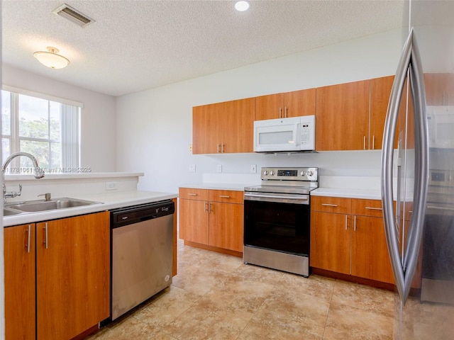 kitchen with a sink, a textured ceiling, brown cabinetry, light countertops, and appliances with stainless steel finishes