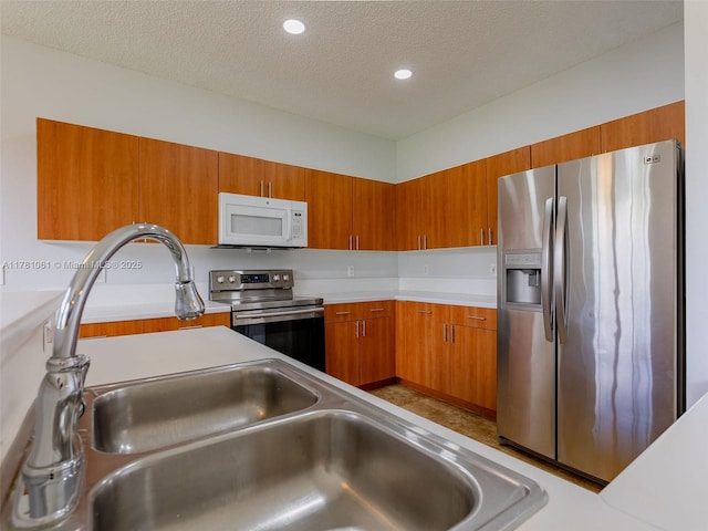 kitchen with stainless steel appliances, a textured ceiling, recessed lighting, brown cabinetry, and light countertops