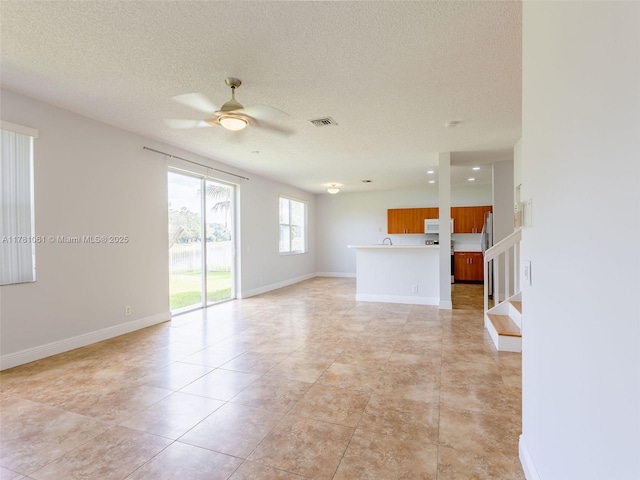 unfurnished living room featuring baseboards, visible vents, a ceiling fan, stairway, and light tile patterned floors