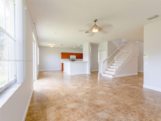 unfurnished living room featuring baseboards, a ceiling fan, stairs, and visible vents