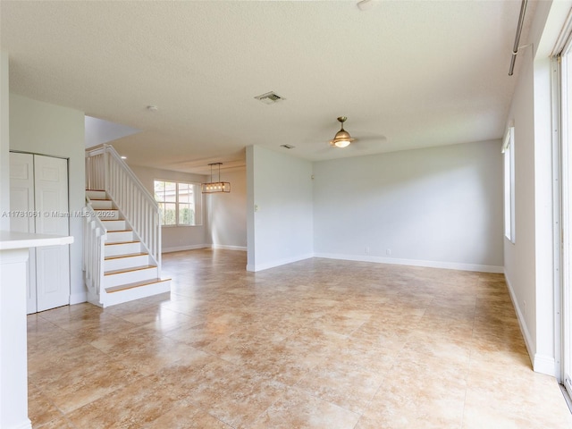 unfurnished room with stairway, visible vents, a ceiling fan, baseboards, and a textured ceiling
