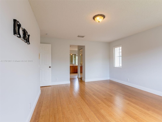 spare room with light wood finished floors, baseboards, a textured ceiling, and visible vents