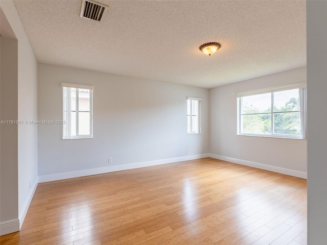 spare room featuring a textured ceiling, light wood finished floors, and visible vents