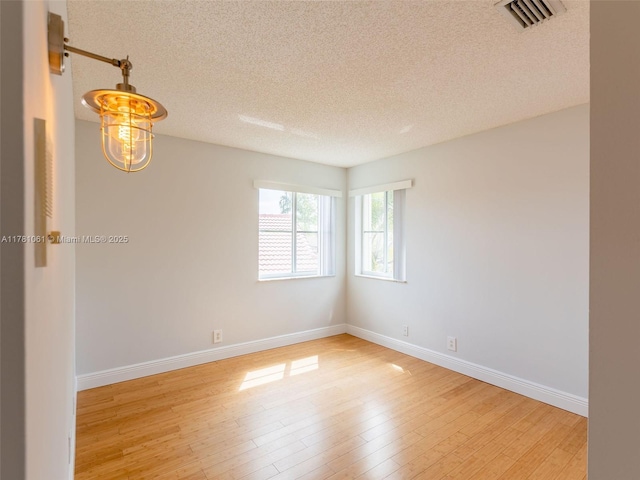 spare room featuring baseboards, wood finished floors, a textured ceiling, and visible vents