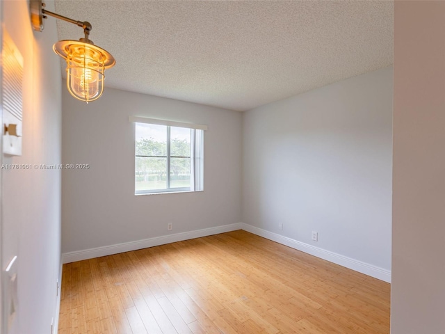 unfurnished room with light wood finished floors, baseboards, and a textured ceiling