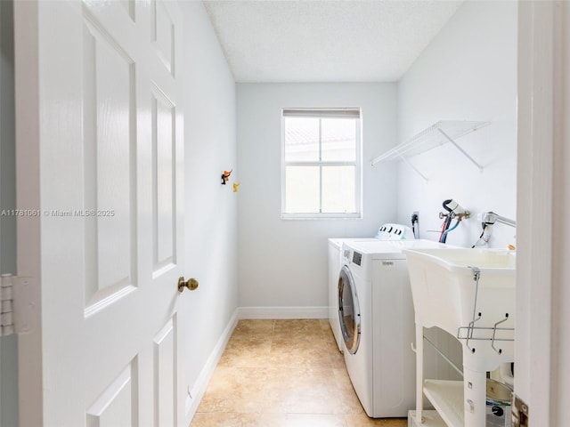 laundry area featuring a textured ceiling, a sink, washing machine and dryer, baseboards, and laundry area