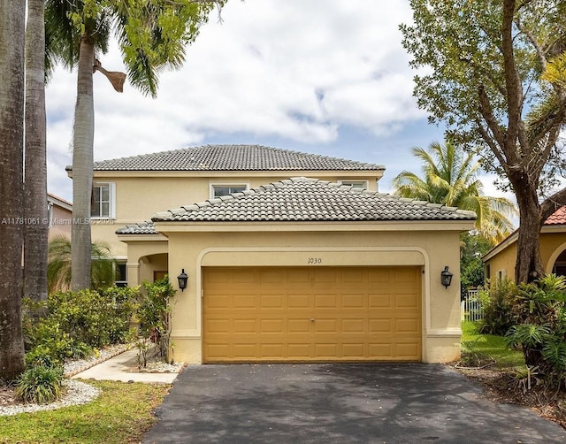 mediterranean / spanish-style house with a garage, a tile roof, aphalt driveway, and stucco siding