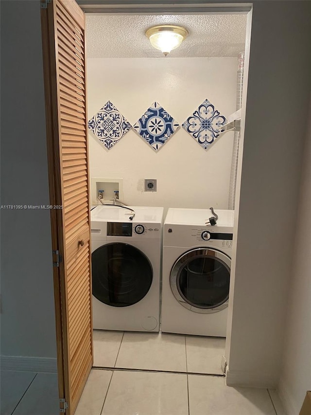 laundry room featuring washer and dryer, light tile patterned flooring, and a textured ceiling
