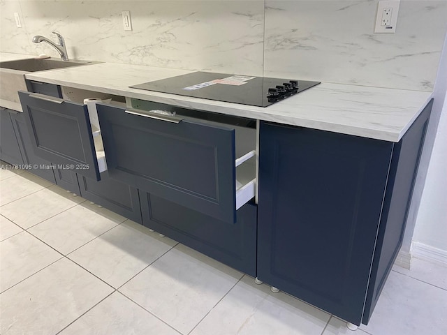 interior details with a sink, blue cabinetry, black electric stovetop, and light stone countertops