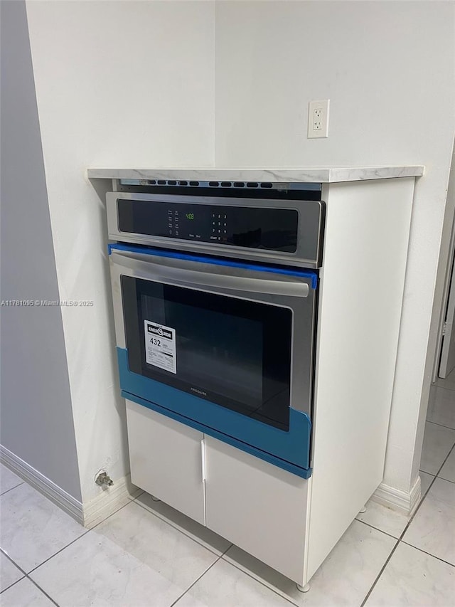 room details with stainless steel oven, light countertops, white cabinetry, and baseboards