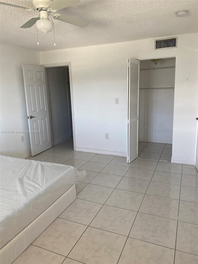 unfurnished bedroom with a closet, a textured ceiling, a ceiling fan, light tile patterned flooring, and visible vents