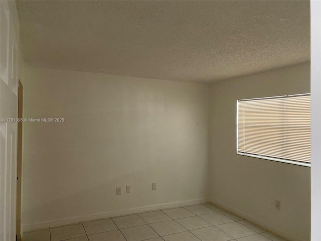 unfurnished room with light tile patterned floors, a textured ceiling, and baseboards