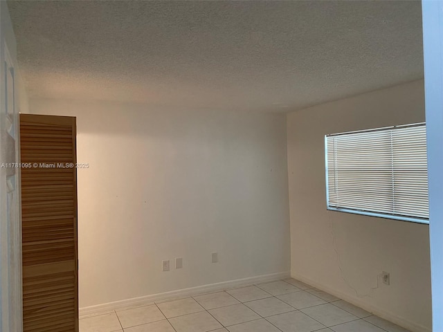 spare room featuring light tile patterned floors, baseboards, and a textured ceiling