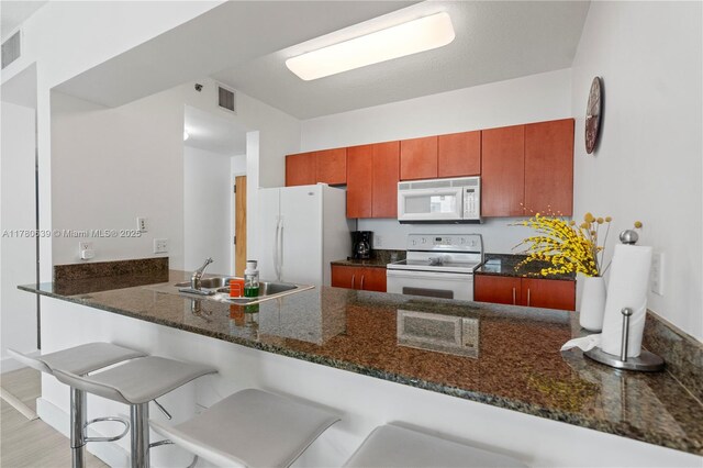 1200 Brickell Bay Dr Ph 4218, Miami, FL 33131 - kitchen with white appliances, a sink, a peninsula, dark stone countertops, and a kitchen bar