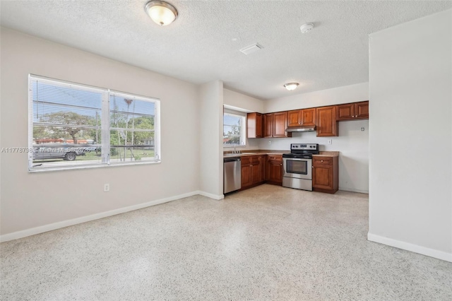 2650 SW 76th Ave, Miami, FL 33155 - kitchen featuring appliances with stainless steel finishes, under cabinet range hood, a textured ceiling, dark aggregate flooring, and brown cabinets
