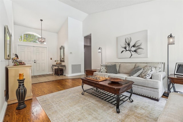 living area with visible vents, baseboards, high vaulted ceiling, and wood finished floors