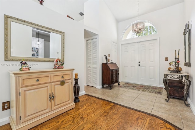 foyer entrance featuring an inviting chandelier, visible vents, light tile patterned flooring, lofted ceiling, and baseboards