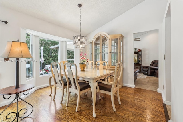 dining space featuring a textured ceiling, wood finished floors, baseboards, and vaulted ceiling