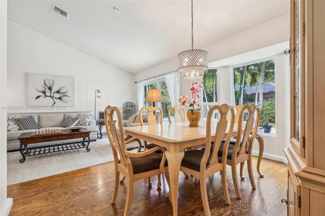 dining space with an inviting chandelier, vaulted ceiling, light wood-style flooring, a textured ceiling, and visible vents