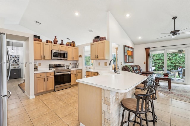 kitchen featuring light tile patterned floors, appliances with stainless steel finishes, a kitchen breakfast bar, a peninsula, and vaulted ceiling