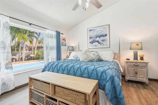 bedroom featuring baseboards, a ceiling fan, a textured ceiling, wood finished floors, and lofted ceiling