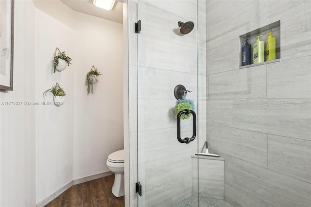 bathroom featuring a shower stall, wood finished floors, baseboards, and toilet