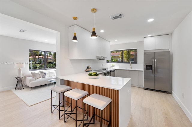 kitchen with a sink, a peninsula, a wealth of natural light, stainless steel fridge, and modern cabinets