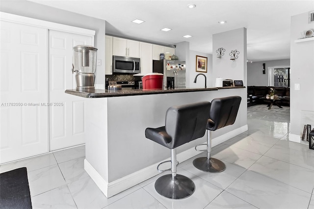 kitchen with baseboards, appliances with stainless steel finishes, backsplash, marble finish floor, and a breakfast bar area