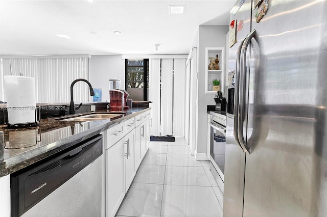 kitchen featuring white cabinetry, dark stone countertops, appliances with stainless steel finishes, marble finish floor, and a sink