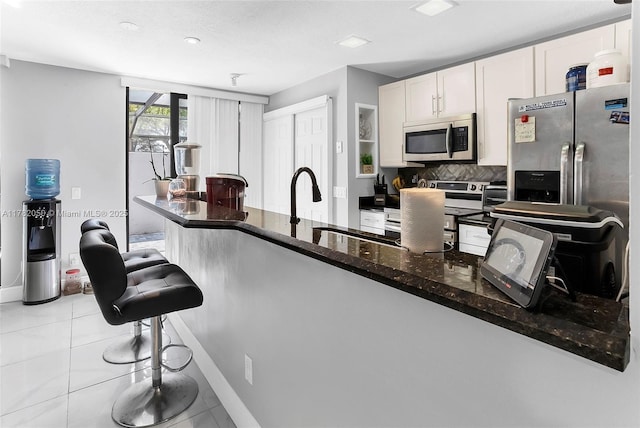 kitchen featuring a kitchen breakfast bar, tasteful backsplash, white cabinetry, dark stone countertops, and appliances with stainless steel finishes