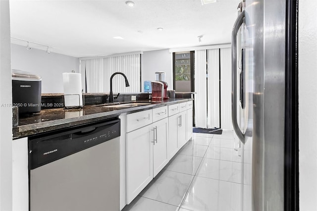 kitchen featuring white cabinetry, dark stone countertops, appliances with stainless steel finishes, marble finish floor, and a sink