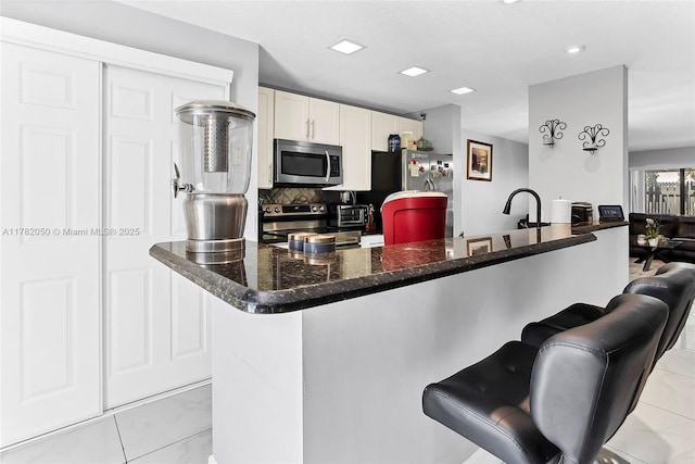 kitchen with tasteful backsplash, white cabinets, a kitchen bar, stainless steel appliances, and marble finish floor