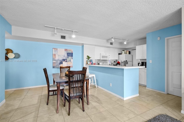 dining room featuring baseboards, track lighting, visible vents, and a textured ceiling