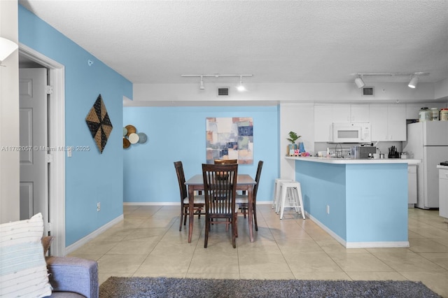 dining space with track lighting, a textured ceiling, and light tile patterned floors