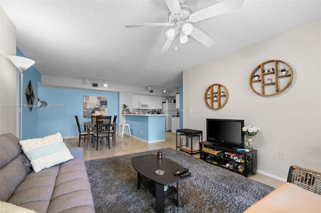 living area featuring rail lighting, a textured ceiling, a ceiling fan, and baseboards