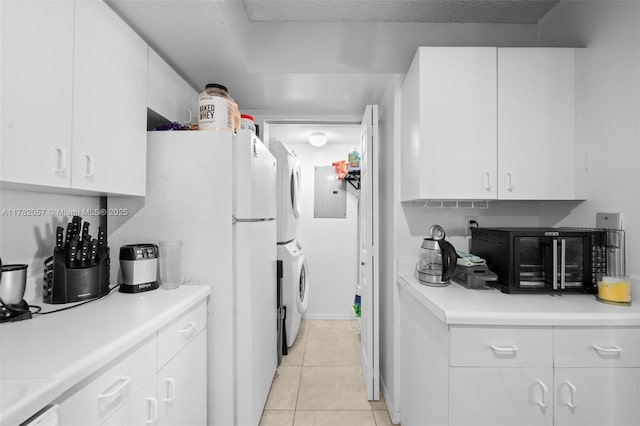kitchen with light tile patterned floors, stacked washer / drying machine, white cabinets, and light countertops