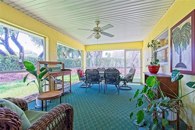 sunroom featuring carpet floors, a ceiling fan, outdoor dining area, and a textured wall