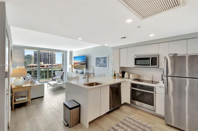 kitchen with a peninsula, open floor plan, visible vents, appliances with stainless steel finishes, and a sink