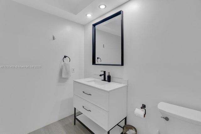 half bathroom featuring recessed lighting, vanity, toilet, and wood finished floors